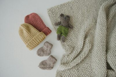 Une collection d'articles tricotés à la main confortables, notamment des bonnets et un ours en peluche sur une surface blanche.