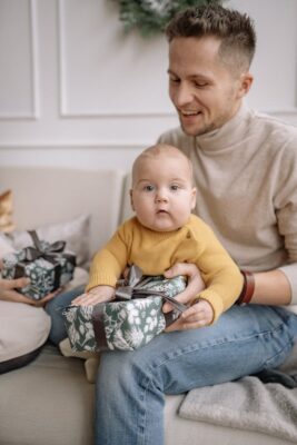 Un père et son bébé assis joyeusement avec des cadeaux de vacances dans un cadre familial chaleureux.