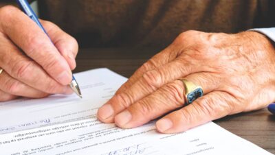 Gros plan d'un adulte âgé signant un document juridique en mettant l'accent sur la main et la bague en or.