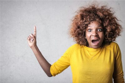 Portrait d'une femme joyeuse pointant vers le haut, exprimant son excitation dans un décor de studio.